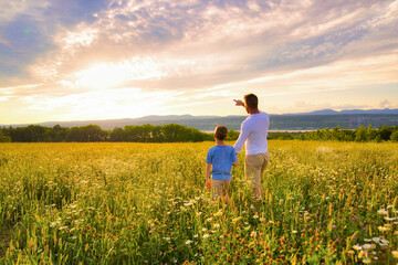 happy family of father and child on field at the sunset having fun pointing something