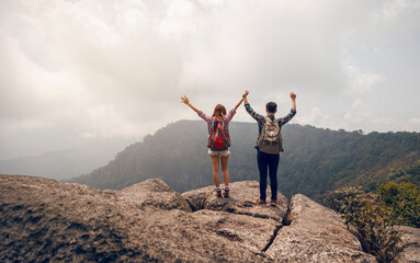 Asian couple hikers with backpacks raised up arms standing on top of mountain, tourist enjoying nature view.