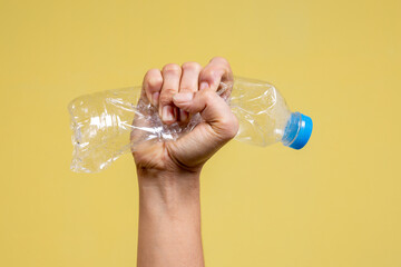 Male hands squeeze plastic bottles isolated on yellow background. Empty plastic bottles recycling waste