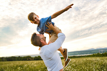 happy family of father and child on field at the sunset having fun flying in the air