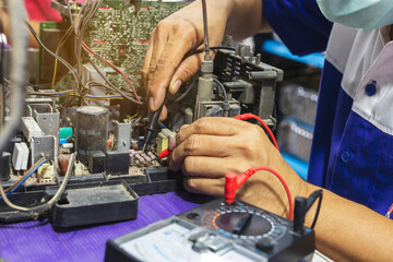 Fototapeta na wymiar Close up of young man technician wearing a mask repairing a television. Repairman are checking television circuit board with multimeter. TV repair service center concept