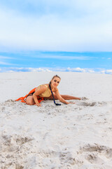 Girls dancers in red skirts and with golden machines in their hands on the beach. White sand and blue sky.