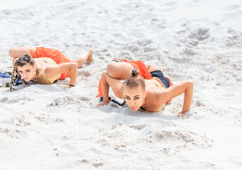 Girls dancers in red skirts and with golden machines in their hands on the beach. White sand and...