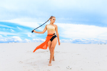 Girls dancers in red skirts and with golden machines in their hands on the beach. White sand and blue sky.