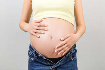 Close up of pregnant belly at colorful background with copy space. Future mother in opened jeans is embracing her naked baby bump. Motherhood concept