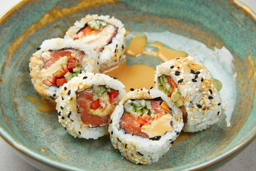 Sushi Uramaki with salmon, seaweed, rolls poured with sauce, sprinkled with sesame seeds, with spices