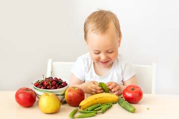 baby boy 2 years old sitting at a table on a white isolated background and eating fruits vegetables, baby food concept, place for text