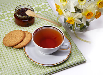 Tea break. Cup of red tea, cookies, marmalade and flowers on light background.