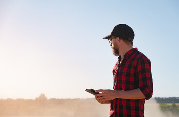 Millennial man with a tablet in a dusty agricultural field. Modern farming, agriculture business,...