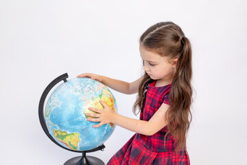 little girl school girl 7 years old sitting in a red dress with a globe on a white isolated background, place for text, September 1, knowledge Day