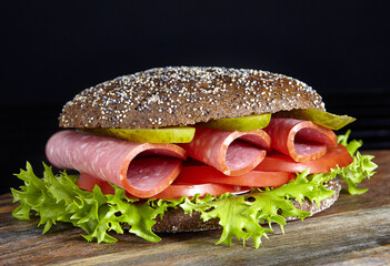 Tasty sandwich with ham, tomatoes, lettuce and sliced pickled cucumbers on a wooden surface. Closeup.