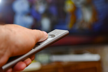 A man holds a remote control in his hand and switches channels to watch TV. Remote control of household appliances.