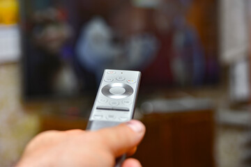 A man holds a remote control in his hand and switches channels to watch TV. Remote control of household appliances.