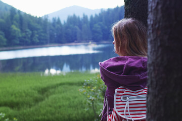 Young caucasian woman hugging a tree in the forest near the lake in summer evening.