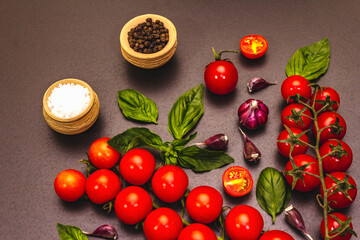 Ripe cherry tomatoes, garlic, basil, salt and black peppercorns on a black stone culinary background