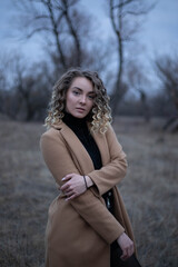 Young beautiful girl with curly hair against the background of the field, black clothes, brown coat, fashion