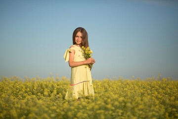 teenage girl in a yellow dress picks flowers in a yellow field in summer