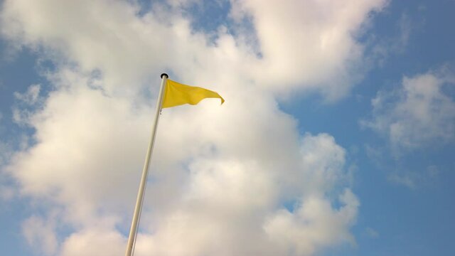 Yellow triangle flag fluttering in the wind against blue sky and clouds at a beach in France. It indicates a medium hazard but supervised swimming area.