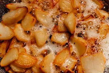 Chunks of potatoes are fried in boiling oil. Close-up photo of cooking junk food.