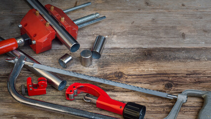 Snapshot of a old wooden workbench in a handicraft workshop with some DIY tools like a silver metal saw, two red pipe cutter and a red vice with a stainless steel pipe and some cut off pipe pieces. 