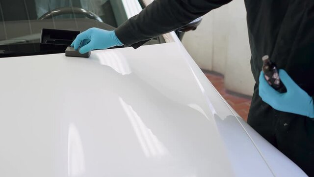 Professional car ceramics worker applies a layer of ceramics to the hood of a car
