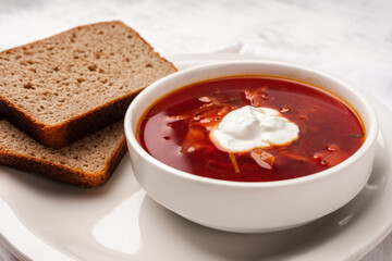 Vegetarian borscht with sour cream in a white tureen next to slices of bread