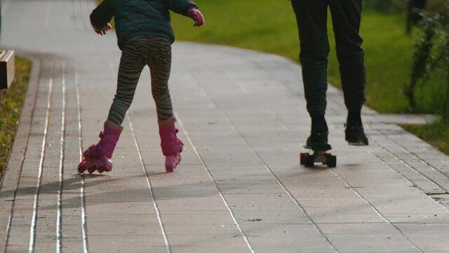Children roller skate and skateboard together in the park on the street