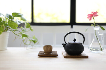 Black traditional teapot with wooden cup and rose flower on pale brown wooden table