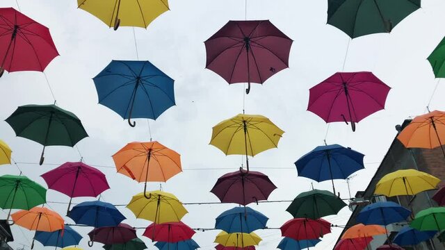 Bright multicolored umbrellas hanging in the sky above the street. The sky above the pedestrian street decorated with vividly colored umbrellas.