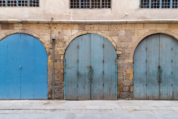 Row of closed three blue weathered wooden arched doors in stone bricks wall, located in old abandoned district