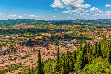 Fototapeta na wymiar A view above the tree line from the Colle Eletto cable car over the cathedral city of Gubbio, Italy towards the Apennine mountains in summer