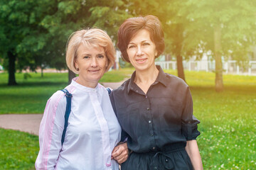 Fototapeta premium Happy positive beautiful LGBT couple of mature women in love walking together in park, holding hands each other, looking at camera, smiling
