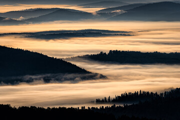 A hazy sunrise in the mountains. Mountains silhouettes and fog in the valleys. Photo from Polonina Wetlinska. Bieszczady National Park. Carpathians. Poland.