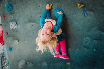 Cute little girl climbing on artificial boulders wall in gym