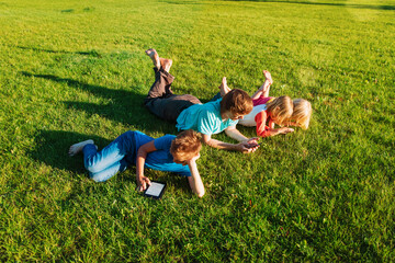 father and kids relax on green grass, family watching smartphones and reading in nature