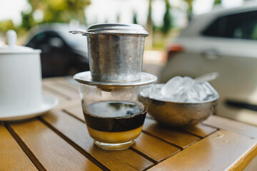 Hot milk coffee dripping in Vietnam style, pouring water over ground coffee contained in Vietnamese Phin Filter on table. Selective Focus.