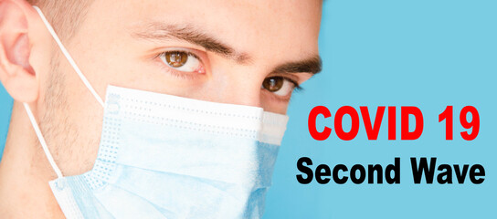 A man in a blue medical mask looks at the camera, sideways. A man in a gray T-shirt on a blue background. Place for text.  Copy Space. Covid-19