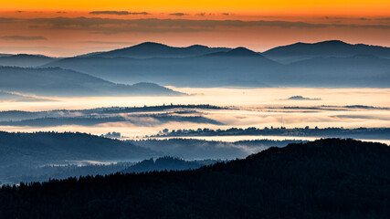 Fototapeta na wymiar A hazy sunrise in the mountains. Mountains silhouettes and fog in the valleys. Photo from Polonina Wetlinska. Bieszczady National Park. Carpathians. Poland.