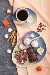 A pieces of homemade chocolate with coconut candies and a cup of coffee on a black concrete background. top view, close up.