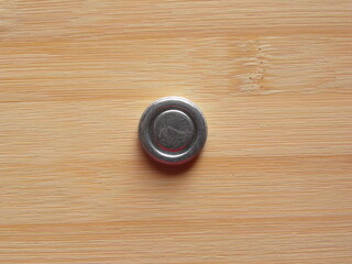 Front side of small silver color round internal magnet of over the ear headphone kept on wooden table