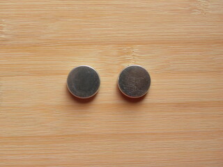 Back side of 2 small silver color round internal magnets of over the ear headphones kept on wooden table