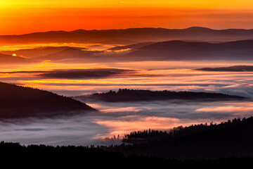 A hazy sunrise in the mountains. Mountains silhouettes and fog in the valleys. Photo from Polonina Wetlinska. Bieszczady National Park. Carpathians. Poland.