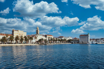 Obraz premium Seaside view of the town of Split, Croatia. Riviera with trees and the old town with the saint dominus cathedral belltower peeking above the buildings. Beautiful blue mid day sky