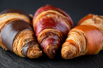 Board with tasty croissants on dark wooden table, closeup. French pastry