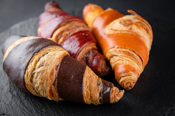 Board with tasty croissants on dark wooden table, closeup. French pastry