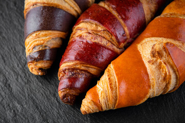 Board with tasty croissants on dark wooden table, closeup. French pastry