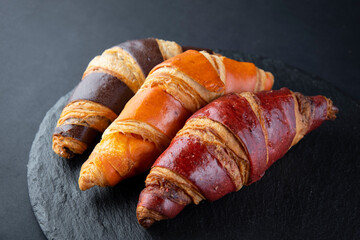 Board with tasty croissants on dark wooden table, closeup. French pastry