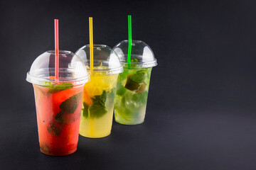 Refreshing summer drink. Colored lemonades,mojito, strawberry in plastic cups with ice on black background. Take away drinks. 