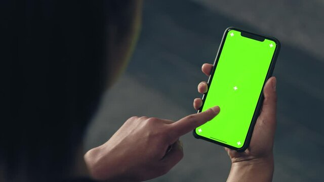 back view of fitness woman using green screen smart phone at home. Woman preparing for workout using smart phone.Woman doing a tap on mobile phone while resting during fitness training