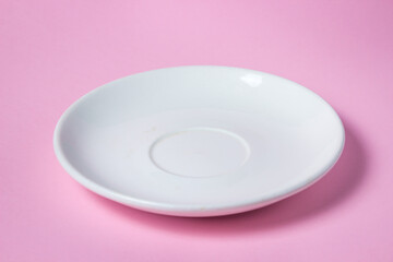 White saucer on a pink background. Empty white porcelain saucer stands on a pink surface